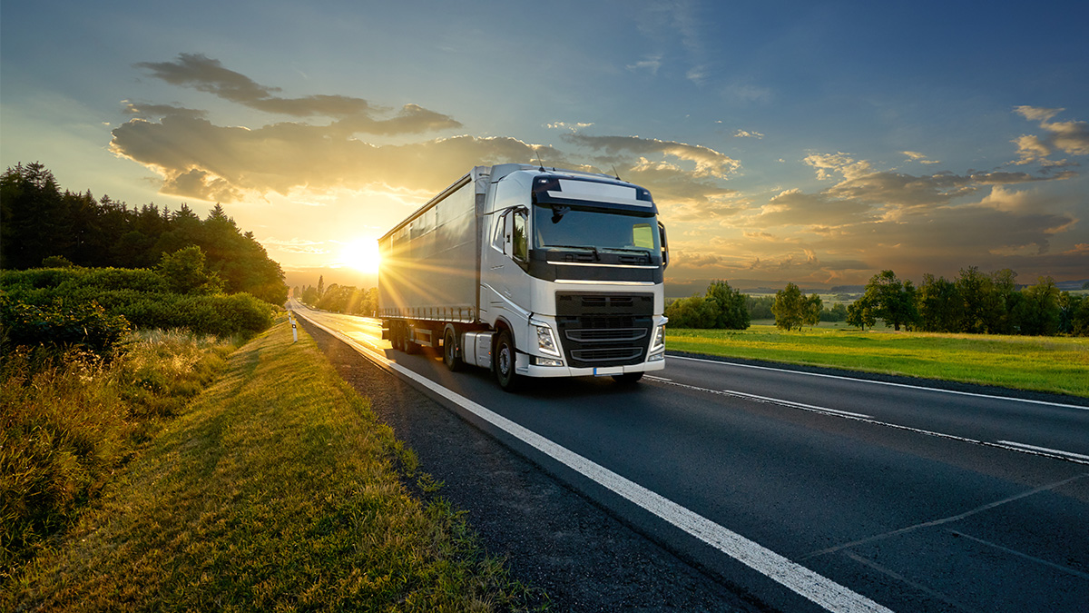 Large semi-truck driving on a highway at sunset with fields and trees on each side